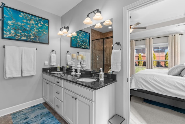 ensuite bathroom with double vanity, tiled shower, a sink, and baseboards