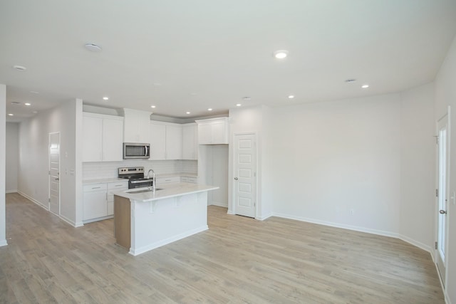 kitchen with tasteful backsplash, white cabinets, appliances with stainless steel finishes, a kitchen island with sink, and light wood-type flooring