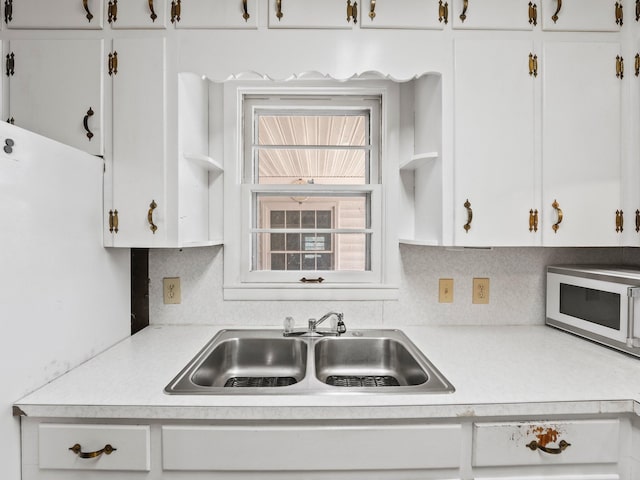 kitchen featuring white cabinets, white microwave, light countertops, and a sink