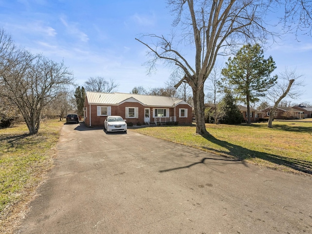 single story home with metal roof, brick siding, a front yard, and driveway