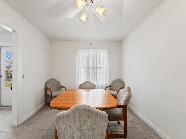 dining area with light carpet, a ceiling fan, baseboards, and crown molding