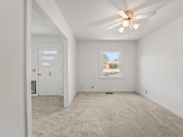 carpeted spare room with crown molding, baseboards, a ceiling fan, and visible vents