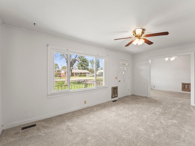 carpeted empty room with visible vents, baseboards, a ceiling fan, and heating unit