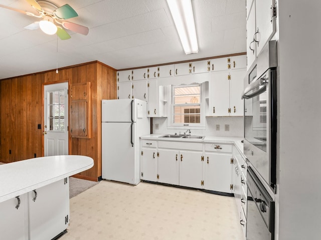 kitchen with freestanding refrigerator, wood walls, stainless steel oven, a sink, and ceiling fan