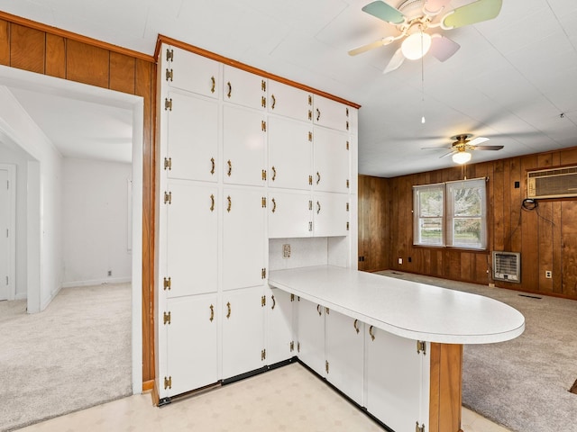 kitchen with a peninsula, wooden walls, a ceiling fan, heating unit, and light colored carpet