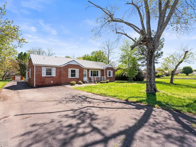 view of front of home featuring an outdoor structure, a front lawn, aphalt driveway, brick siding, and metal roof