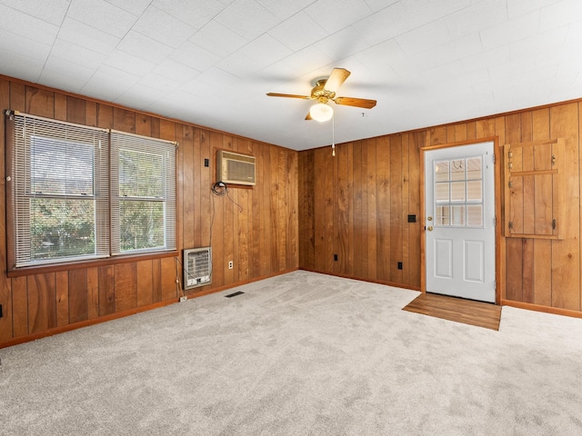 carpeted spare room featuring a wall unit AC, a ceiling fan, visible vents, wooden walls, and heating unit