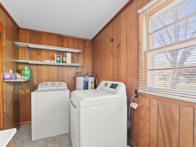 clothes washing area featuring water heater, washing machine and clothes dryer, laundry area, and wooden walls