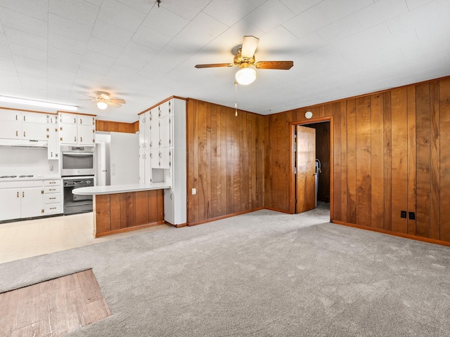 unfurnished living room featuring wooden walls, ceiling fan, light carpet, and baseboards