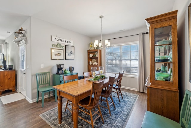 dining space featuring dark wood-type flooring, a notable chandelier, and baseboards