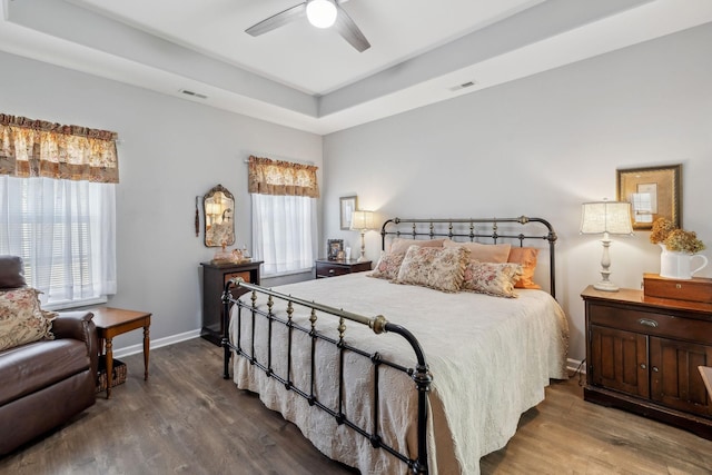 bedroom featuring baseboards, visible vents, a raised ceiling, and wood finished floors