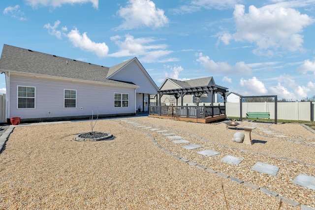 back of house featuring roof with shingles, fence, a deck, and a pergola