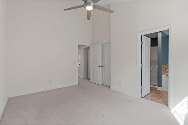 unfurnished bedroom with baseboards, ensuite bath, ceiling fan, a high ceiling, and carpet floors