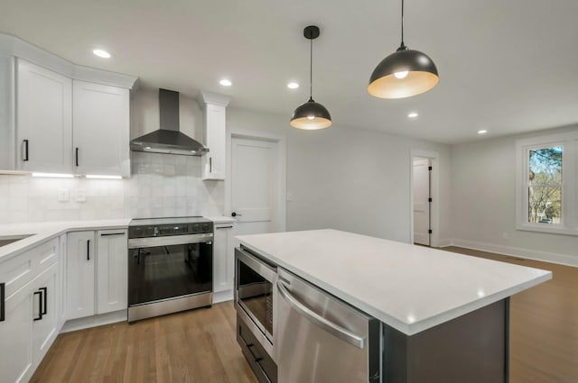 kitchen with stainless steel appliances, light countertops, light wood-style floors, and wall chimney range hood