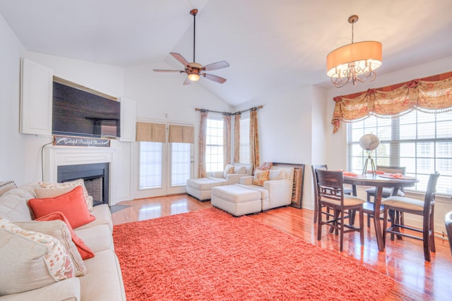 living room featuring light wood-style floors, lofted ceiling, a fireplace, and ceiling fan with notable chandelier