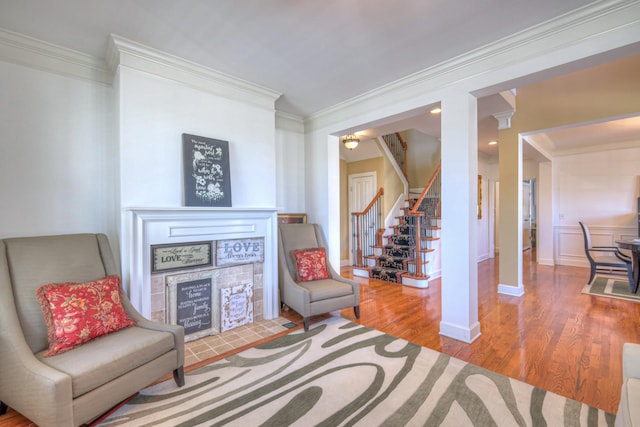 living area with a fireplace with flush hearth, wood finished floors, baseboards, stairs, and ornamental molding