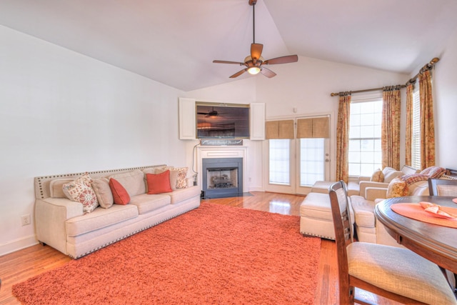 living area featuring lofted ceiling, light wood-style flooring, a fireplace with flush hearth, a ceiling fan, and baseboards