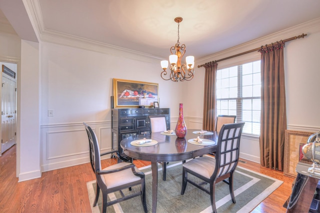 dining room featuring a wainscoted wall, wood finished floors, crown molding, a chandelier, and a decorative wall