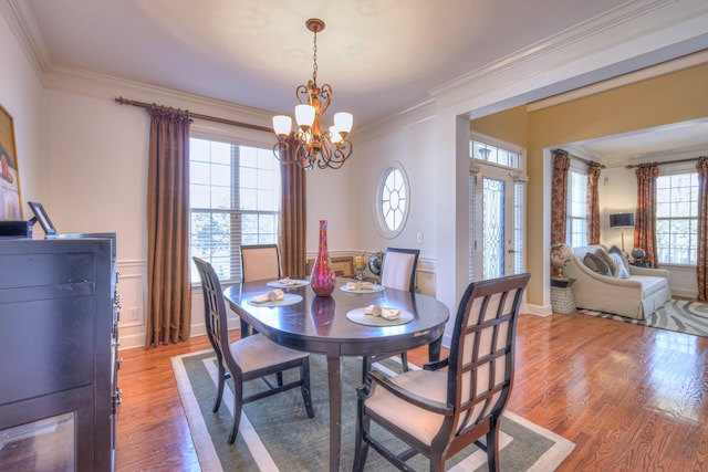 dining room featuring light wood-type flooring, a notable chandelier, baseboards, and crown molding