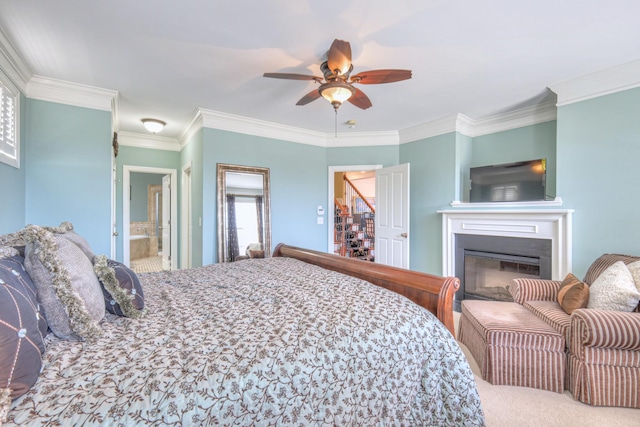 carpeted bedroom featuring ensuite bath, ornamental molding, ceiling fan, and a glass covered fireplace