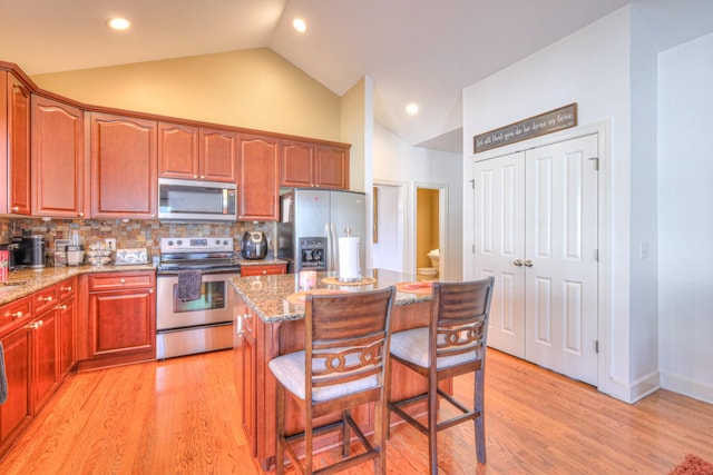 kitchen with stainless steel appliances, light stone counters, a kitchen bar, and light wood-style floors