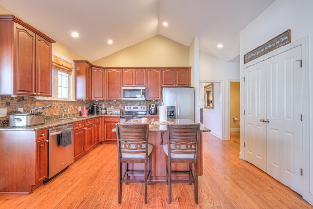 kitchen with a breakfast bar area, appliances with stainless steel finishes, a sink, a kitchen island, and light wood-type flooring