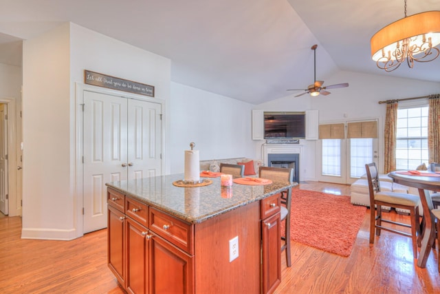 kitchen with lofted ceiling, stone countertops, a fireplace, light wood-type flooring, and a center island