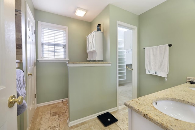 full bathroom featuring double vanity, baseboards, a walk in closet, and a sink