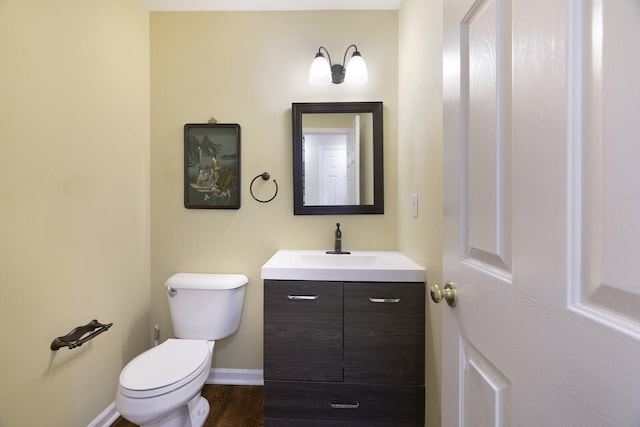 half bathroom with wood finished floors, vanity, toilet, and baseboards