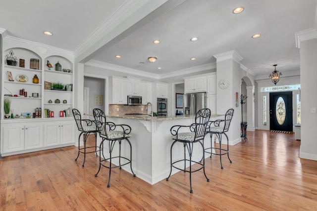 kitchen with light stone counters, arched walkways, a breakfast bar area, appliances with stainless steel finishes, and white cabinetry