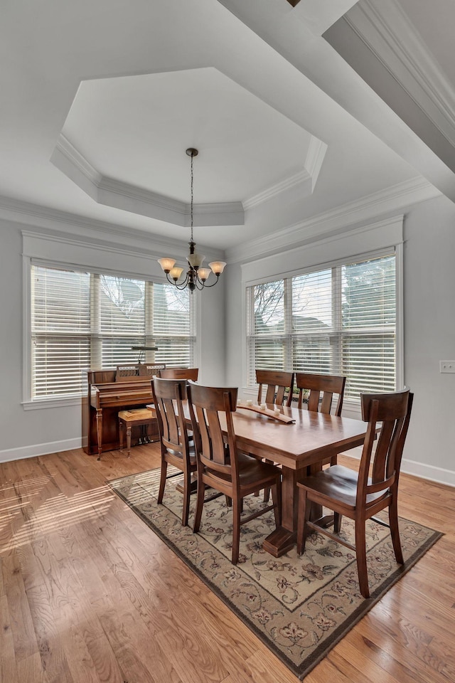 dining space featuring crown molding, a tray ceiling, light wood-style floors, and a notable chandelier