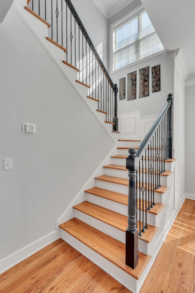 staircase with ornamental molding, baseboards, and wood finished floors