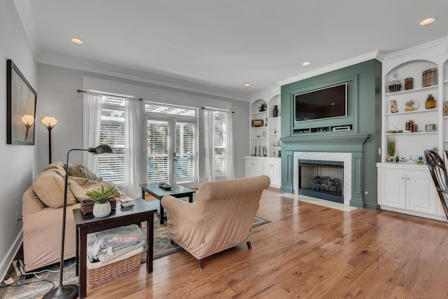 sitting room featuring built in shelves, crown molding, recessed lighting, light wood-style flooring, and a fireplace with flush hearth