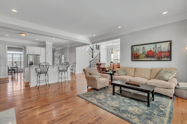 living room with a healthy amount of sunlight, crown molding, light wood-style flooring, and stairs