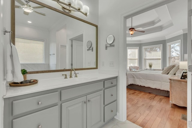 bathroom with ceiling fan, connected bathroom, wood finished floors, a tray ceiling, and crown molding