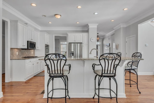 kitchen featuring stainless steel appliances, white cabinetry, light wood-style flooring, and a breakfast bar area