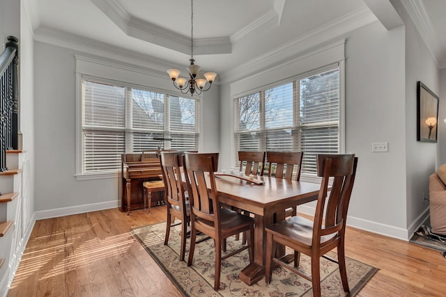 dining space with light wood-style floors, a tray ceiling, a notable chandelier, and ornamental molding