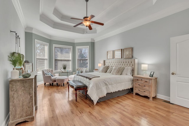 bedroom featuring ornamental molding, a tray ceiling, light wood-type flooring, and baseboards