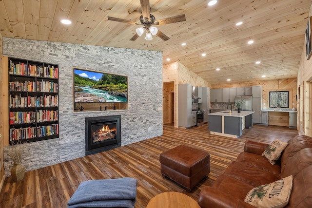 living area featuring built in features, wooden ceiling, wood finished floors, vaulted ceiling, and a stone fireplace