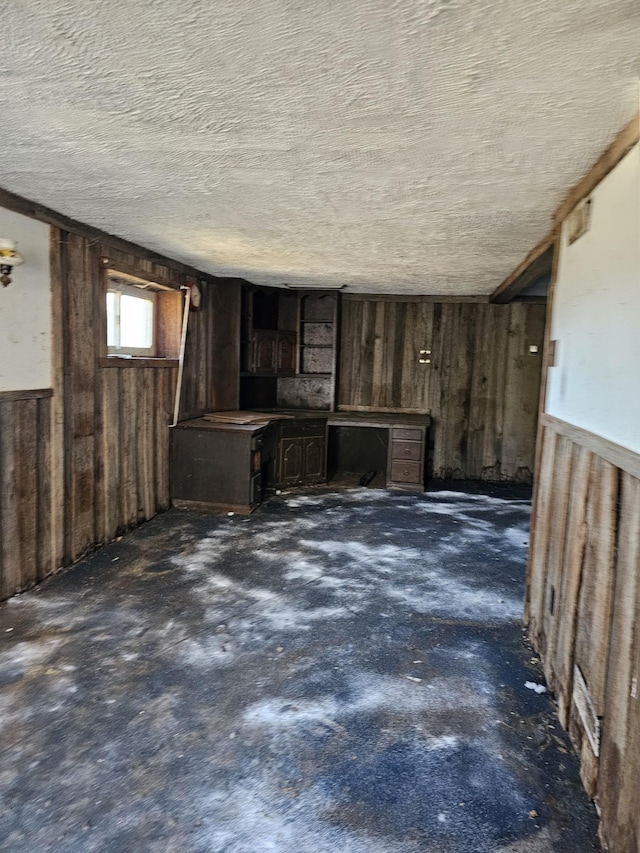 interior space with wooden walls, a textured ceiling, and wainscoting