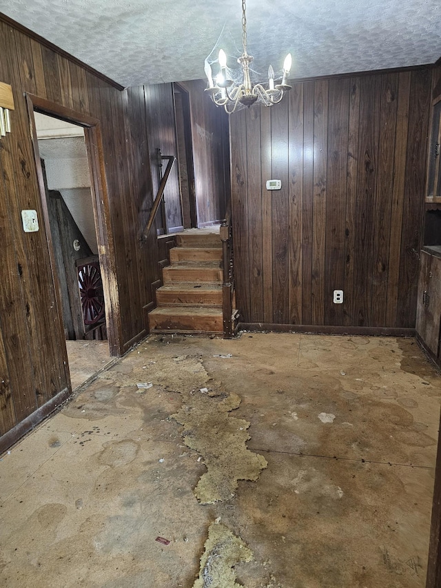 empty room with a chandelier, wood walls, a textured ceiling, and stairs