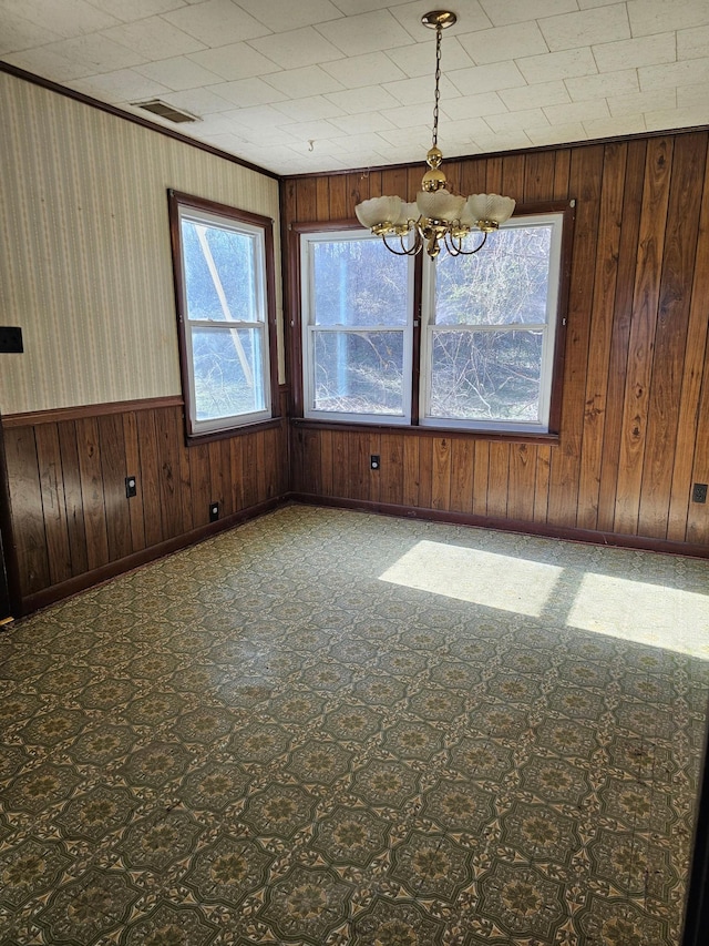 empty room with a wainscoted wall, wood walls, visible vents, and an inviting chandelier