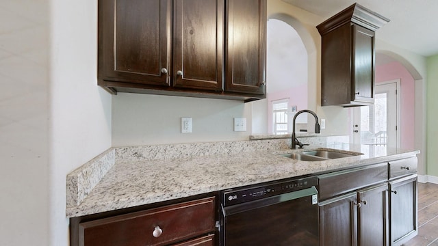 kitchen featuring dark brown cabinetry, black dishwasher, arched walkways, light stone counters, and a sink