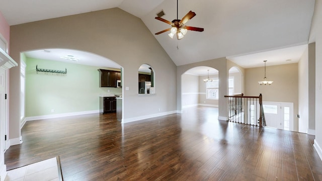 unfurnished living room with arched walkways, high vaulted ceiling, ceiling fan with notable chandelier, dark wood-type flooring, and baseboards