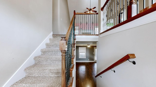 stairs with ceiling fan, a high ceiling, and wood finished floors