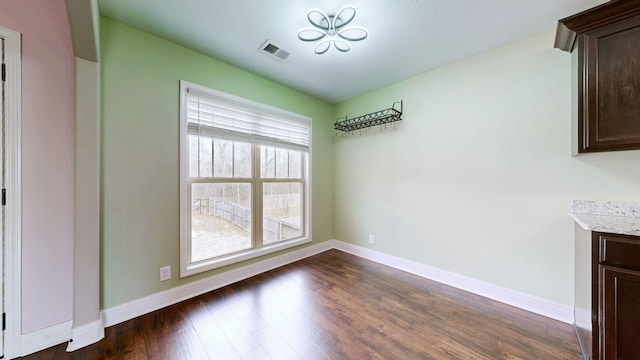 unfurnished dining area with dark wood-type flooring, visible vents, and baseboards