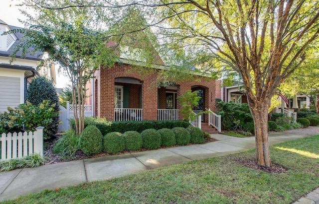 view of front facade featuring a porch, brick siding, and fence