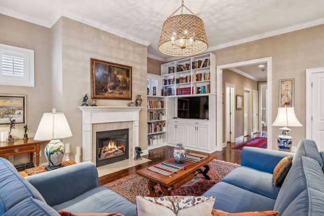 living room with a notable chandelier, a fireplace with flush hearth, wood finished floors, baseboards, and ornamental molding