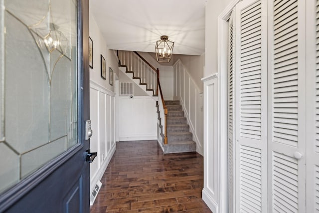 entrance foyer featuring a decorative wall, dark wood finished floors, stairway, a wainscoted wall, and a notable chandelier