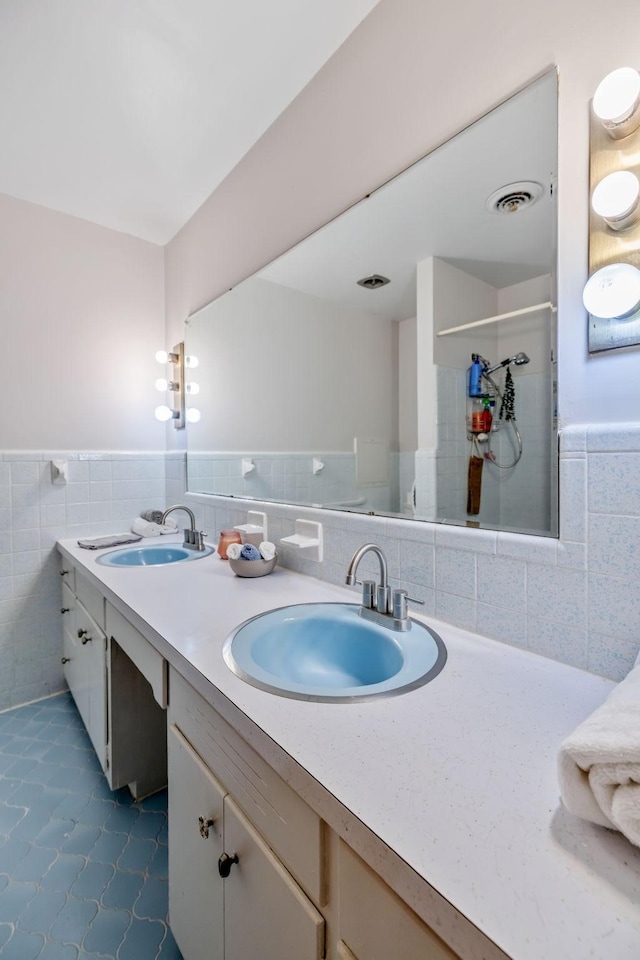 full bath with tile walls, tiled shower, visible vents, and a sink